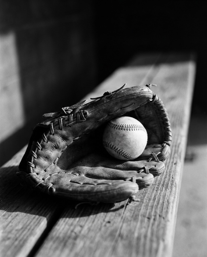 A worn baseball glove and ball on a dugout bench